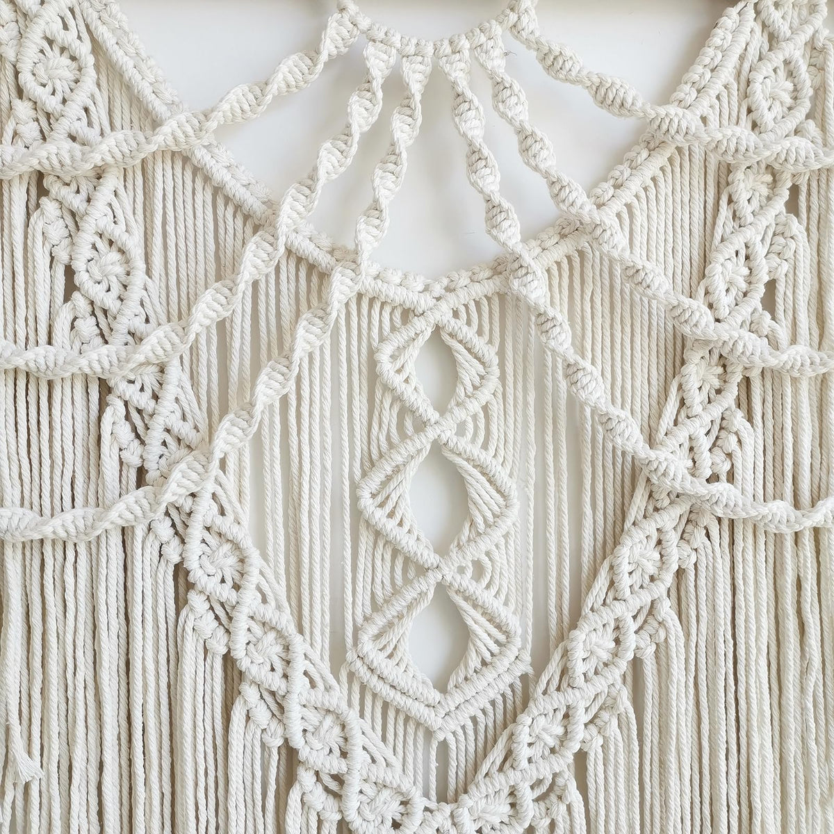 Achart macrame wall hanging above bed creates a cozy bedroom focal point.