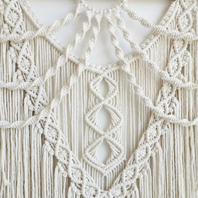 Achart macrame wall hanging above bed creates a cozy bedroom focal point.