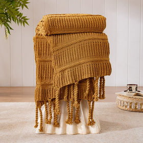 Down Home Boho knitted chenille blanket with tassels in amber brown over a cozy living space for comfortable warmth