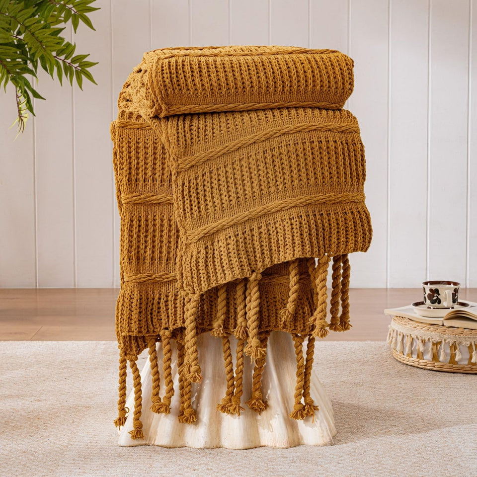 Down Home Boho knitted chenille blanket with tassels in amber brown over a cozy living space for comfortable warmth