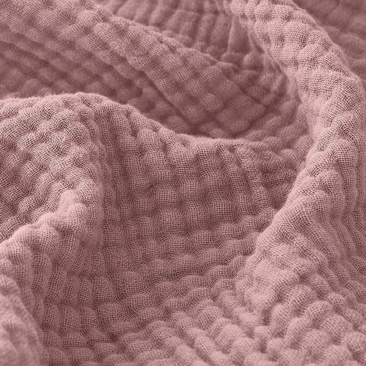EMME muslin throw blanket in dusty pink on couch for cozy warmth.