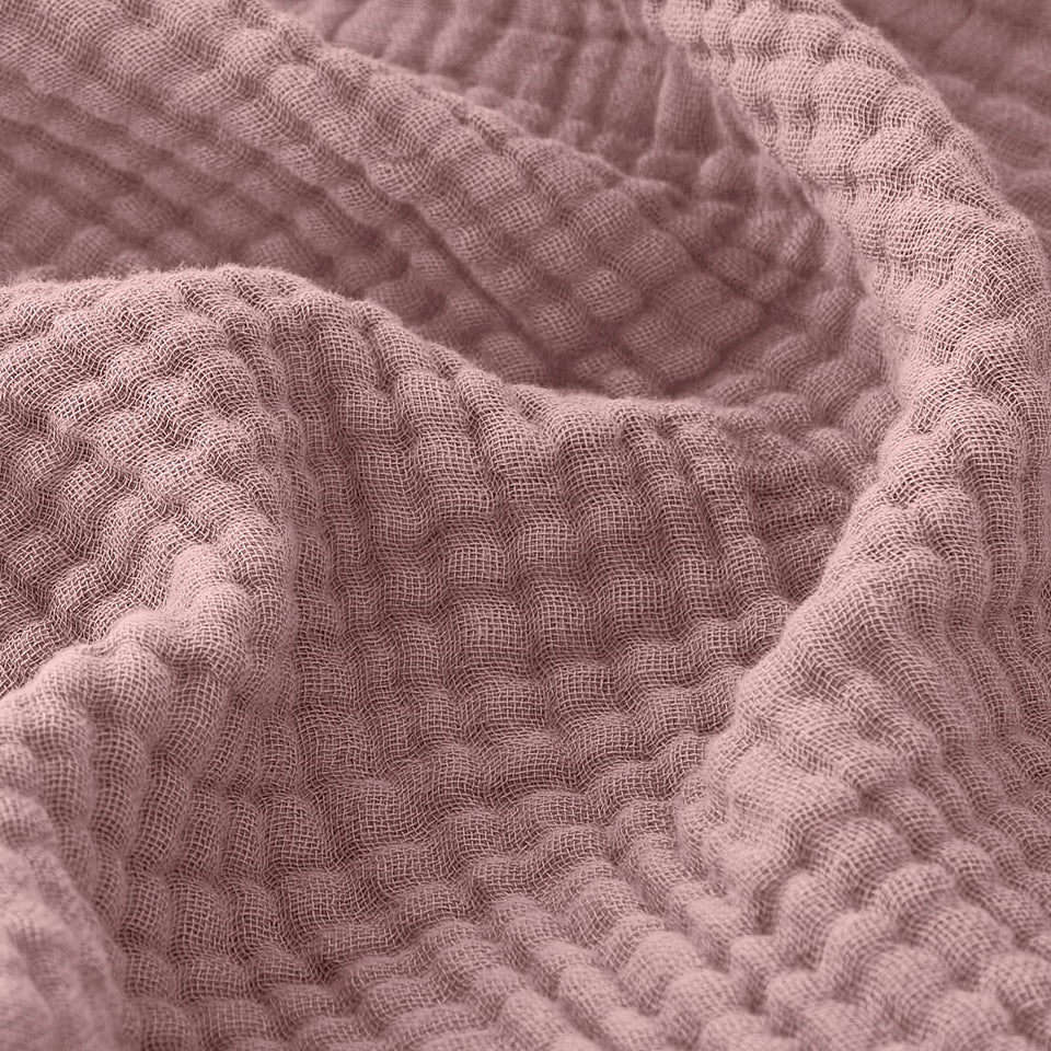 EMME muslin throw blanket in dusty pink on couch for cozy warmth.