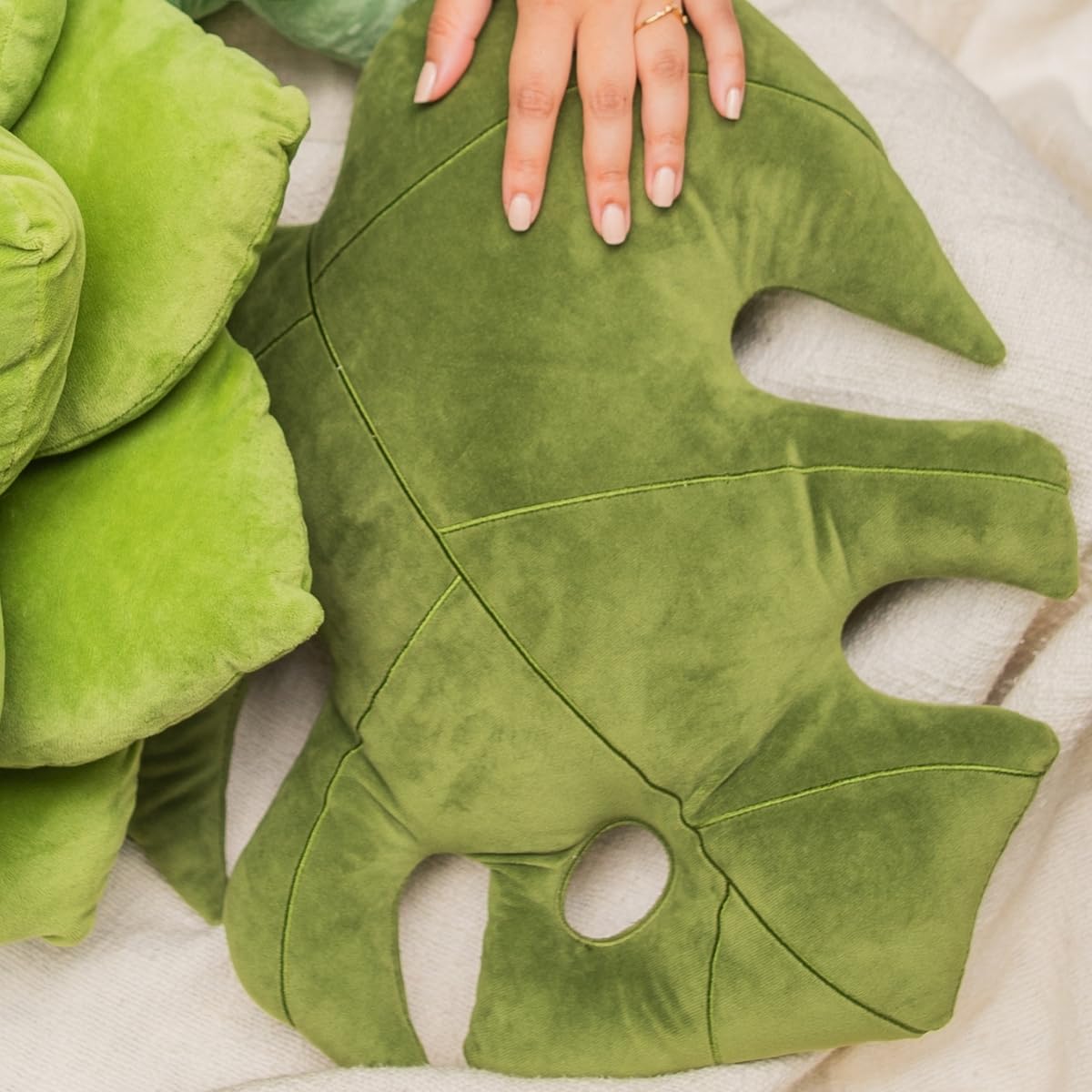 Green Philosophy Co. Monstera Leaf Pillow on couch provides plush support for neck and back.
