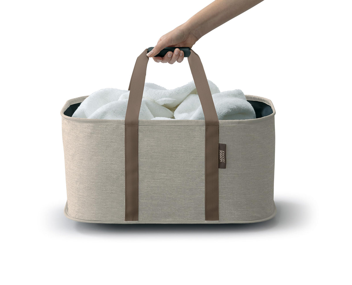 Joseph Joseph Hold-All full-load laundry scene highlights easy one-handed carrying.