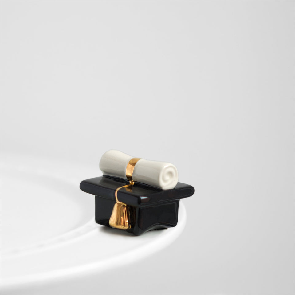 Nora Fleming Top of Class graduation cap mini enhances desk display for celebrations.