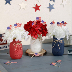 Three colorful mason jars centerpieces with artificial flowers for patriotic events.