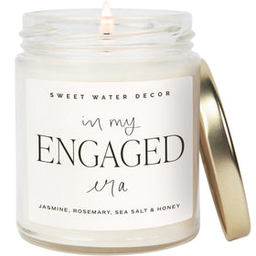 Sweet Water Decor Engaged Era Candle jar enhances cozy decor with warm glow.
