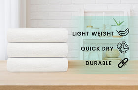 Zuperia white bath towels stacked, bulk pack ideal for large facilities.